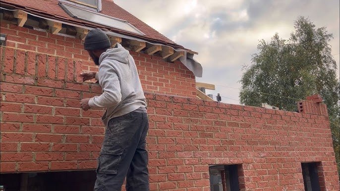 Mason rebuilding and repointing brick parapet wall on a Westchester brownstone roof